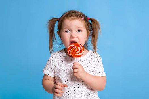 Beautiful little female child holding huge lollipop spiral candy smiling happy isolated on blue background. In children loving sweet and caramel concept