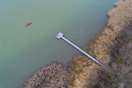 Top view of man in red kayak beside private wooden dock in cold frozen river on winter day