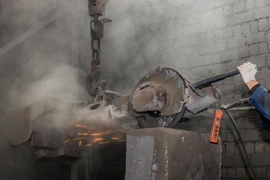 Heavy grinding equipment suspended on a chain with a hook processes and cleans cast iron reinforced concrete tubing in the workshop of an industrial plant.