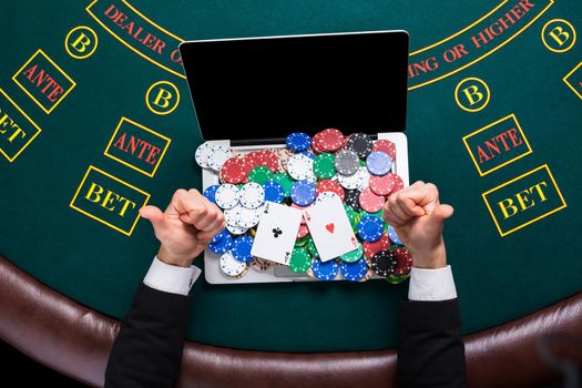 casino, online gambling, technology and people concept - close up of poker player with playing cards, laptop and chips at green casino table. top view. in the hands of two aces, a winning combination