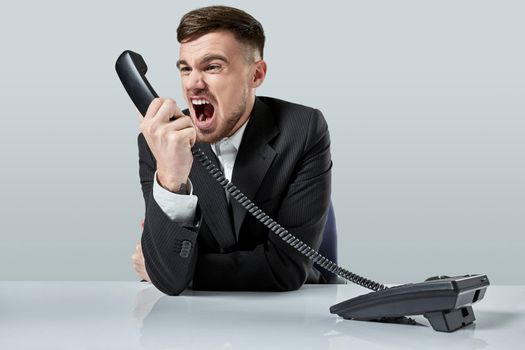 A young man in a black suit dials the phone number while sitting in the office. Manager talking on the phone. Man emotionally shouts