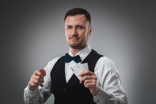 Young man in shirt and waistcoat shows his cards and holds poker chips in his hands, studio shot. Poker. Emotions