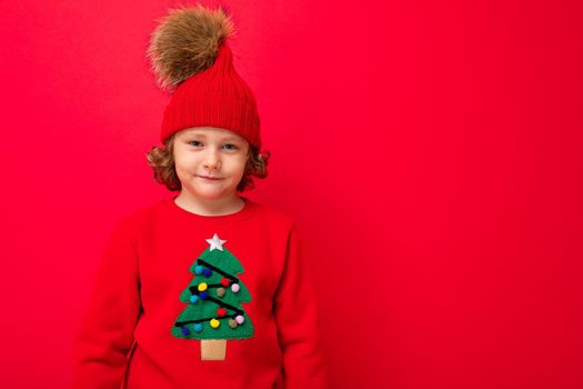 boy model on a red background, portrait of a cool blonde with curls in a sweater with a Christmas tree.