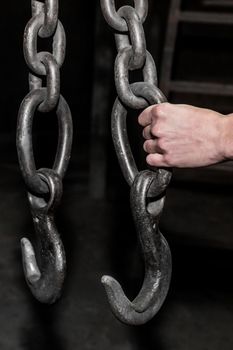 The hand of a man worker holds an iron chain with a hook lifting mechanism of a crane in an industrial plant.