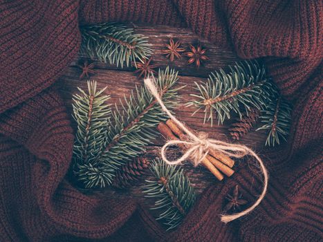 Christmas composition of spruce branches, knitted sweater, cinnamon, anise and cones on rustic wooden background. Cosy and soft winter background in warm, trendy colors. Flat lay, top view