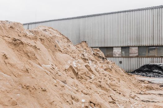 A large pile of sand of natural industrial material is stored outdoors on the territory of the plant.