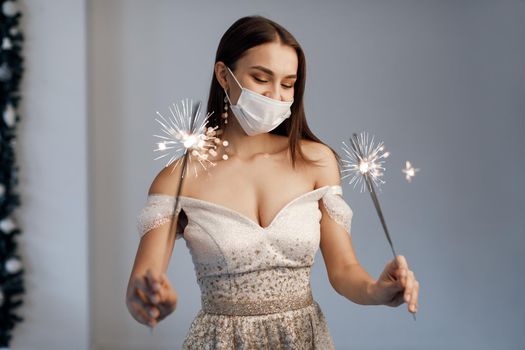 Young woman with sparklers and champagne. New Year covid, woman in dress in mask. High quality photo