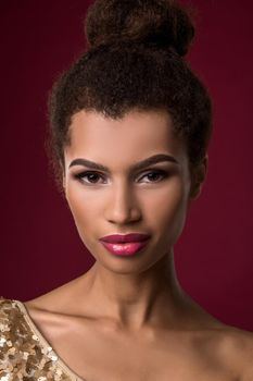 Fashion young African woman with makeup, in short sexy gold dress. Model on a red background in the studio