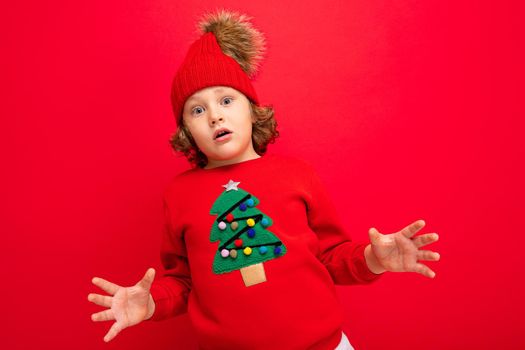 cool boy with curls on a red background in a sweater with a christmas tree.