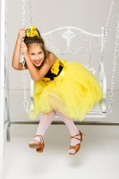 Beautiful little girl swinging in the studio on a swing. Concept of a happy childhood, family well-being.