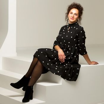 A beautiful young woman is sitting in a studio on a white staircase. Style and fashion concept.