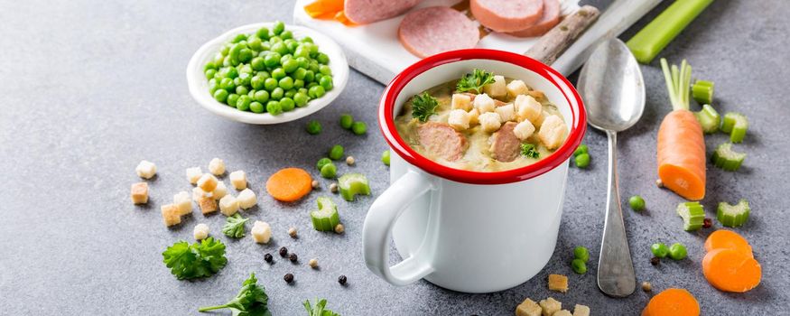 White enamel mug with delicious homemade pea soup with sausage and croutons. Healthy food concept.