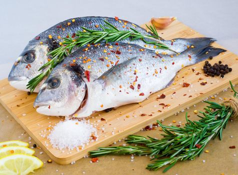 Mediterranean seafood concept. Raw dorado fish with lemon, spices and rosemary on wooden board. Fresh organic sea bream or dorada fish.