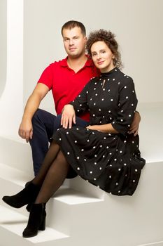 Beautiful family man and woman are sitting on the white stairs in the studio. The concept of love, friendship.