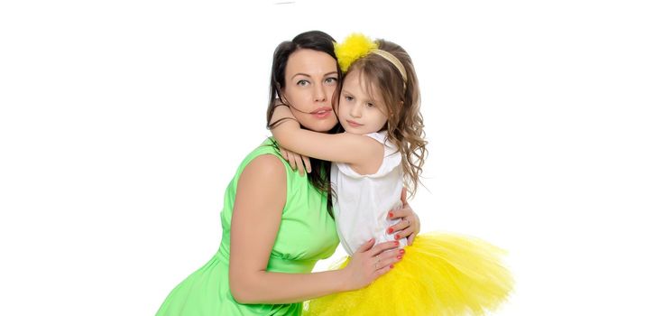 Beautiful young mother in a short green dress and her little beloved daughter in a yellow skirt.Daughter gently hugs the mother's neck.Isolated on white background.