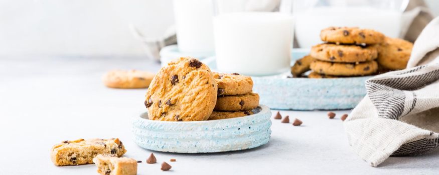 Chocolate chip cookies on blue stone plate with glass of milk on light gray background. Selective focus. Copy space.