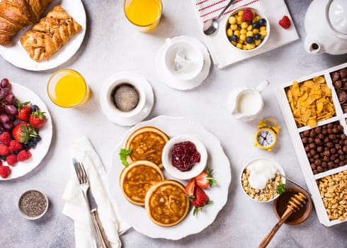 Healthy breakfast for two with coffee, pancakes, fresh berries, quick cereals and orange juice on light gray background, top view.