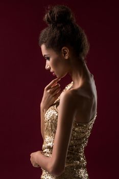 Fashion young African woman with makeup, in sexy gold dress. Model on a red background in the studio. A woman is half a turn