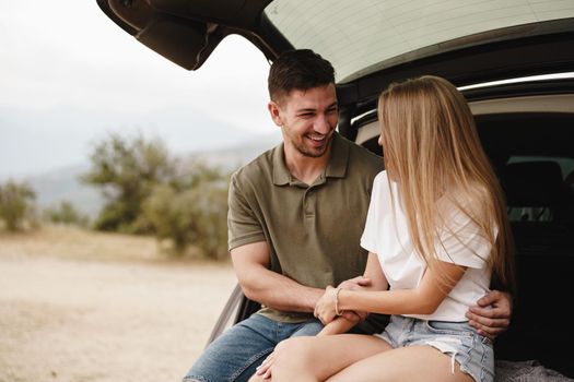 Young happy couple on a road trip sitting in car trunk outdoor