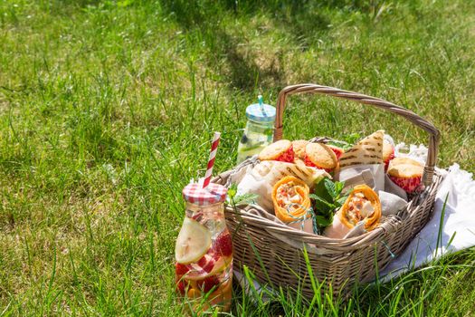 Picnic basket with food on green sunny lawn. Healthy eating.
