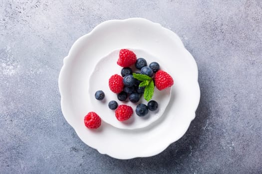 Freshly picked blueberries and raspberries on white plate on gray stone background. Concept for healthy eating and nutrition with copy space. Top view.