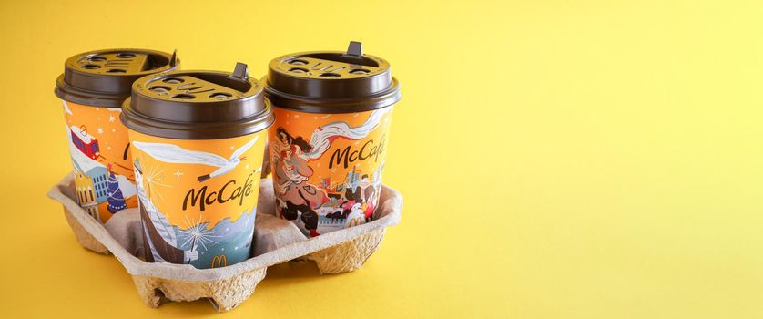 Ukraine, Kyiv - November 1, 2021: Coffee to go background. Yellow glass of coffee from McDonald's copy space. Different winter glass drink McCafe. Cocoa cup on table menu in fastfood restaurant banner