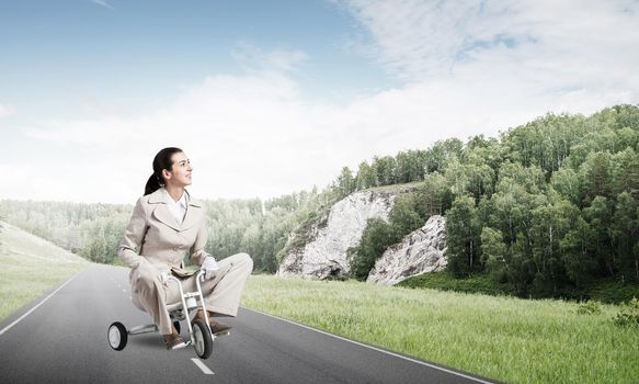 Beautiful caucasian woman riding kid's bicycle on asphalt road. Young employee in white business suit biking outdoor. Professional career start. Beginner level concept with female bicyclist.