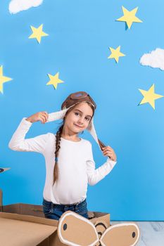 Little child girl in a pilot's costume is playing and dreaming of flying over the clouds. Portrait of funny kid on a background of bright blue wall with yellow stars and white clouds