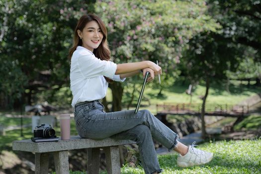 Image of pleased positive woman sitting outdoors in park and using tablet