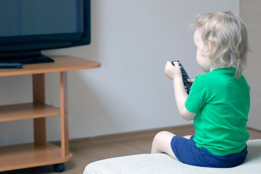 A child with a remote control in his hand turns on the TV to watch cartoons.