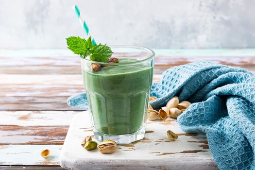 Healthy green smoothie with mint, pistachios and spirulina in glass on old wooden background. Detox, diet, healthy, vegetarian food concept with copy space.