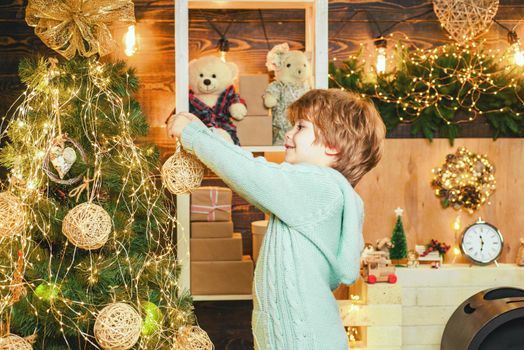 Child in Christmas dress decorating Christmas tree with baubles and having fun at home