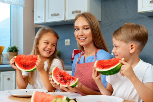 Sweet family, mother and her kids eating watermelon in their kitchen having fun, close up