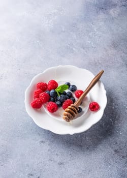 Freshly blueberries and raspberries on white plate with honey. Healthy eating and nutrition concept with copy space.