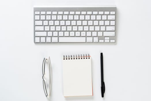 Top view of businessman workplace. Spiral notepad, glasses and computer keyboard on white surface. Education, creativity and working concept with copy space. Finance and investment background.