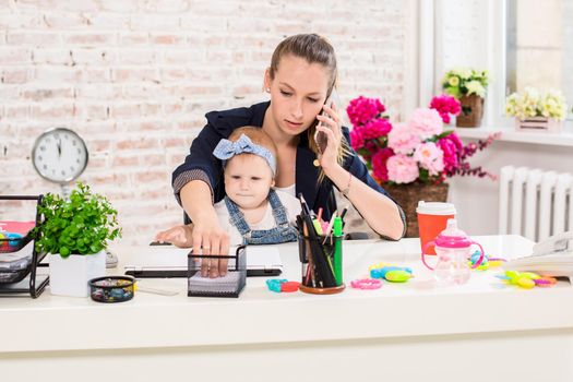 Family Business - telecommute Businesswoman and mother with kid is making a phone call. At the workplace, together with a small child