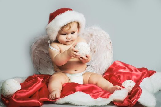 Baby Christmas. Cute funny angel infant with wings in a Santa hat