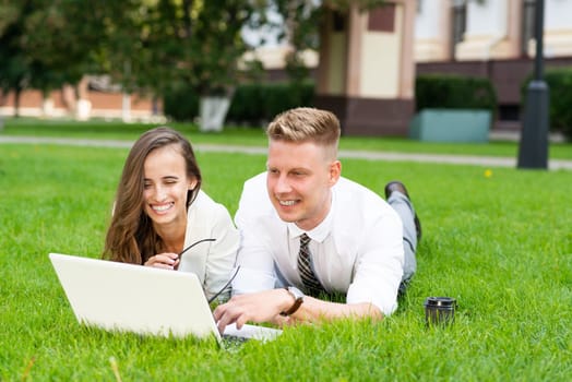 man and woman work with a laptop on grass in park. Business-building concept