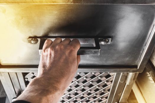 A person's hand opens the handle of an iron cabinet or drawer.