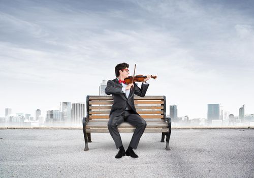 Young businessman plays the violin sitting on a wooden bench. Inspiration in business