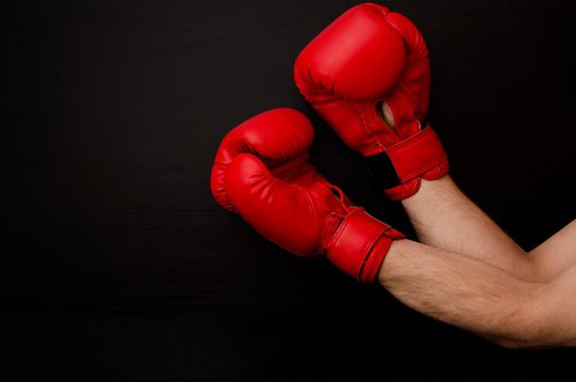 Hand in red boxing gloves in the corner of the frame on a black background, empty space