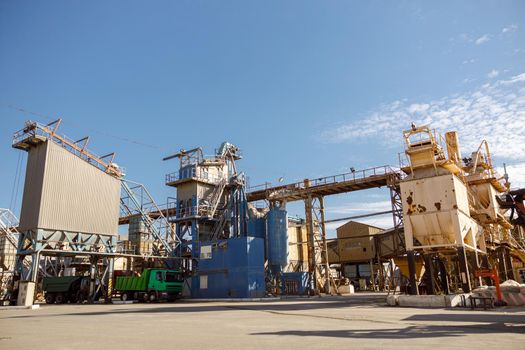 Manufacturing plant with buildings, industrial cranes, ladders and trucks under cloudy sky