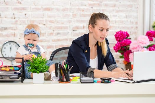 Businesswoman mother woman with a daughter working at the laptop. At the workplace, together with a small child