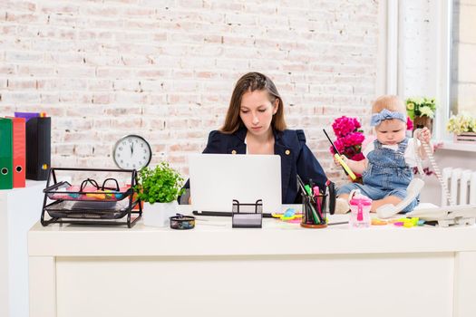 Businesswoman mother woman with a daughter working at the computer. At the workplace, together with a small child