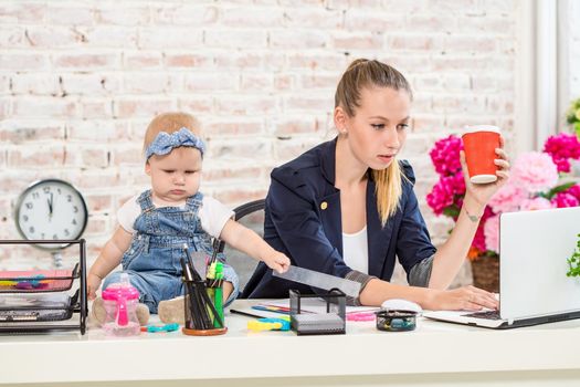 Businesswoman mother woman with a daughter working at the laptop. At the workplace, together with a small child