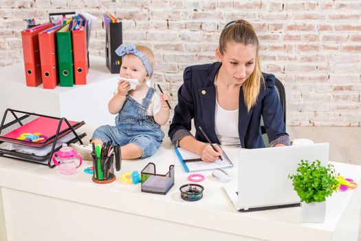 Businesswoman mother woman with a daughter working at the laptop. At the workplace, together with a small child