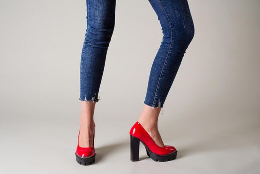 Woman in jeans red shoes with black heels posing on a gray background. - image