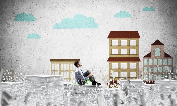 Thoughtful businessman looking away while sitting among flying letters with drawn cityscape on background. Mixed media.