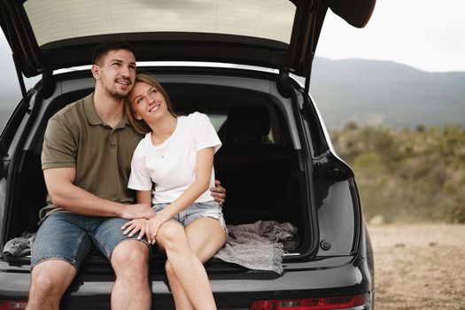 Young happy couple on a road trip sitting in car trunk outdoor