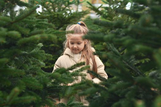 Small girl chooses a Christmas tree in the shop.